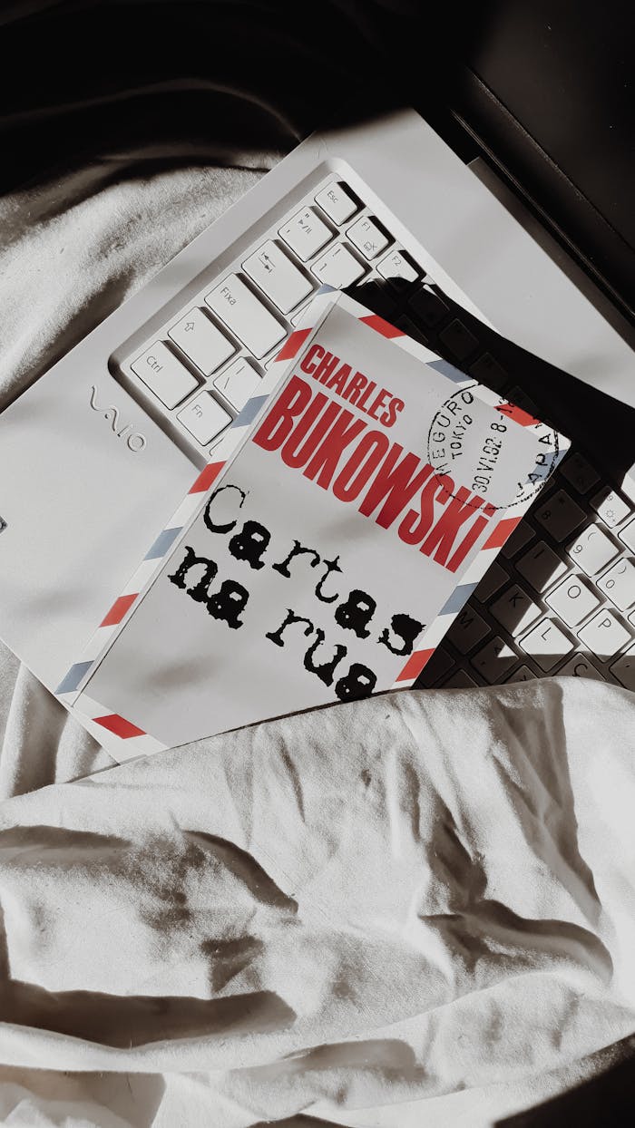 A book titled Cartas na rua by Charles Bukowski lying on a keyboard with white bedding.