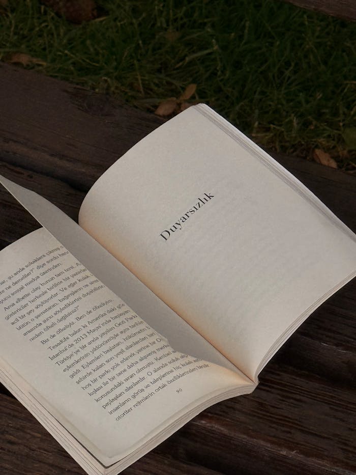 An open book on a wooden bench in an outdoor setting, pages turning.